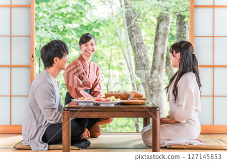 A female inn staff member explaining the dishes in a guest room at a hot spring inn 127145853