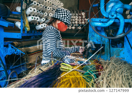 Vietnamese female weaver works on a loom in a workshop at a factory producing traditional woven reed mats in Vietnam in Asia 127147999