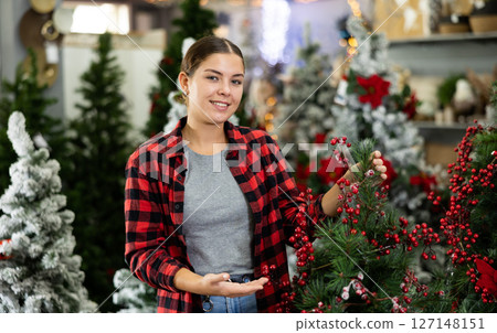 Female seller decorating an artificial Christmas tree with red holly berries at Christmas market 127148151