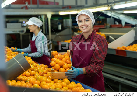 Smiling young female fruit warehouse worker with box of mandarins 127148197