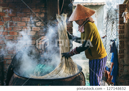 Vietnamese woman in a traditional straw hat dyes reeds at a woven mat factory in Vietnam Vietnamese woman in a traditional straw hat dyes reeds at a woven mat factory in Vietnam 127148632
