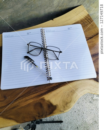 Open notepad with pen and glasses on wooden table. A Blank Sheet Of Notebook With The Items Of A Businessman. Ideal for branding and note-taking app presentations. Close up Open notepad with pen and glasses on wooden table. A Blank Sheet Of Notebook With The Items Of A Businessman. Ideal for branding and note-taking app presentations. Close up 127149718