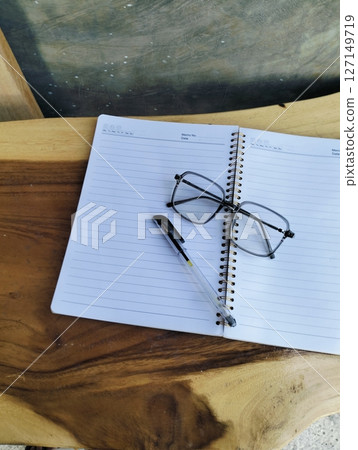 Open notepad with pen and glasses on wooden table. A Blank Sheet Of Notebook With The Items Of A Businessman. Ideal for branding and note-taking app presentations. Close up Open notepad with pen and glasses on wooden table. A Blank Sheet Of Notebook With The Items Of A Businessman. Ideal for branding and note-taking app presentations. Close up 127149719