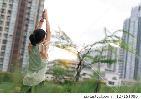 Asian woman wellness from fitness yoga workout. stretching exercise reduces medical shoulder pain inflammation and muscle strain injury risk. Urban city healthcare promotes wellness at sunset 127151080