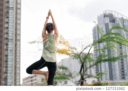Asian woman finds wellness with fitness yoga. workout stretching exercise in an urban city at sunset reduces shoulder pain muscle strain inflammation and medical injury risk for total healthcare 127151082