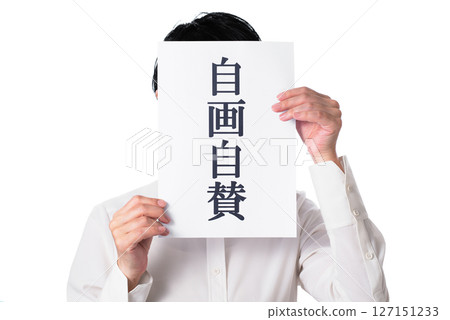 A person wearing a white shirt holding a piece of paper with the words "Self-praise" written on it 127151233