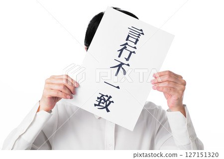 A person wearing a white shirt holding a piece of paper that reads "Inconsistent behavior" 127151320