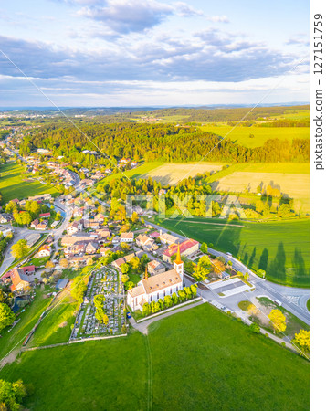 Bohutin Town showcases a picturesque landscape with lush fields and quaint homes. The historic church and cemetery are prominent features, illuminated by the warm glow of sunset. Bohutin Town showcases a picturesque landscape with lush fields and quaint homes. The historic church and cemetery are prominent features, illuminated by the warm glow of sunset. 127151759