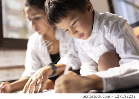 Asian child drawing with pen and paper, mother helping with homework 127152232