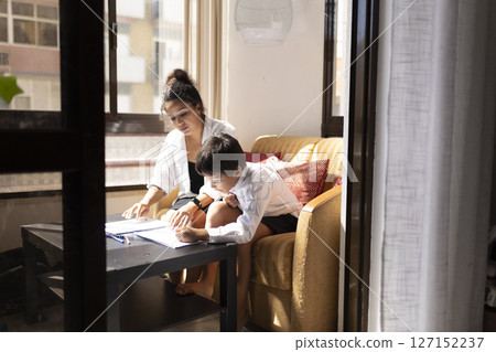 Mother helping son with homework in living room 127152237