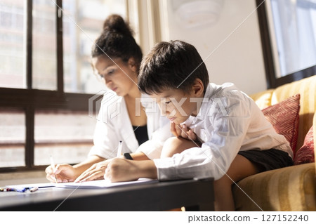 Mother and son sitting on a sofa and writing on a notebook 127152240