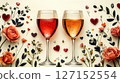 Two elegant wine glasses, one filled with red wine and the other with sparkling rose, are surrounded by painted roses, leaves, and heart shaped decorations, evoking a romantic and artistic ambiance. 127152554