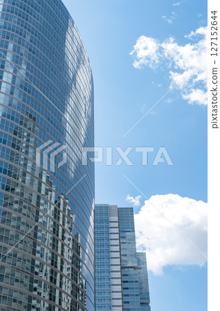 A skyscraper against a blue sky with clouds reflected in the windows 127152644