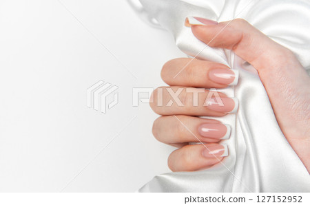 Woman hand showing french manicure on white silk background 127152952
