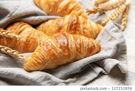 Freshly baked croissants resting on a linen cloth with wheat stalks 127152959