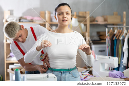 Professional qualified male dressmaker taking measurements of woman client for tailoring in sewing workshop Professional qualified male dressmaker taking measurements of woman client for tailoring in sewing workshop 127152972