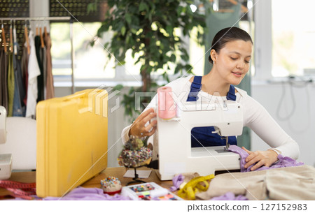 Repairwoman master is collecting and testing sewing machine after repairing sitting at table in sewing workshop 127152983