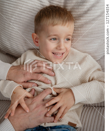 Close-up of a 4-year-old boy's face laughing from tickling his dad at home on the couch. High quality photo 127154854