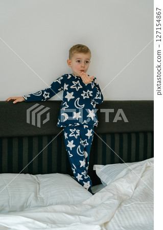 a little blond-haired boy in blue pajamas in his parents' bed lounging in the white sheets. High quality photo 127154867