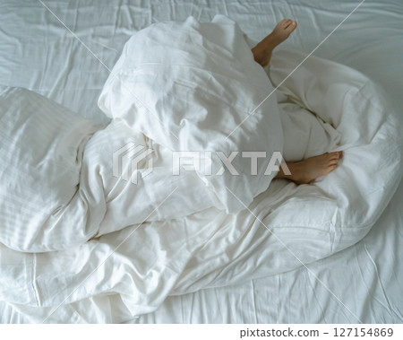 The feet of a small child in a parent's bed on white sheets rolled in a white blanket . High quality photo 127154869