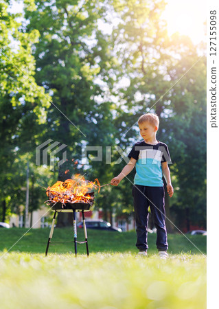 Cute little adorable baby boy put wooden stick in fire pit with huge fire at city park or house yard. Child play dangerous game with bonfire. Fire accident risk and health damage concept 127155098