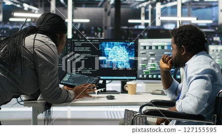 Admin in wheelchair and data center coworker working together using AI node tree software to minimize downtime. Server hub IT expert in disability and colleague using visual programming app, camera B 127155595