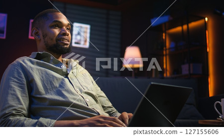 Portrait of african american adult typing data on his laptop at home, being self employed relaxing on a bean bag. Young person working remotely on freelancing tasks, casual teleworker. Camera A. Portrait of african american adult typing data on his laptop at home, being self employed relaxing on a bean bag. Young person working remotely on freelancing tasks, casual teleworker. Camera A. 127155606