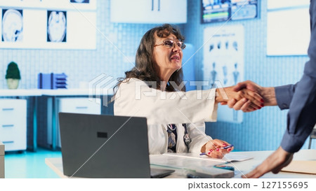 Senior physician consulting an old male patient and gives advice, analyzing the diagnostic report to provide the correct treatment. Utilizing medical technology for care management. Camera A. Senior physician consulting an old male patient and gives advice, analyzing the diagnostic report to provide the correct treatment. Utilizing medical technology for care management. Camera A. 127155695