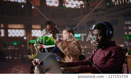 Young adult listening to study music and writing ideas for bachelor paper, using ambient sounds to help with concentration in the campus library. Girl student does academic research. Camera B. Young adult listening to study music and writing ideas for bachelor paper, using ambient sounds to help with concentration in the campus library. Girl student does academic research. Camera B. 127155759