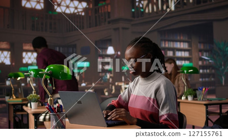 African american student consulting academic research collection at library, studying for upcoming exams to obtain her university diploma. Girl works on a scholarship, education. Camera B. African american student consulting academic research collection at library, studying for upcoming exams to obtain her university diploma. Girl works on a scholarship, education. Camera B. 127155761