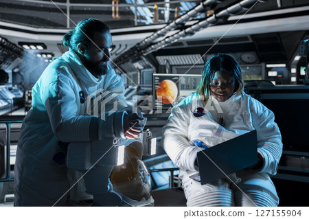 Teamworking astronauts use tablet to ensure safe operation during long distance space travel to Mars. Orbital station crew monitors system stability during cosmic journey to red planets 127155904