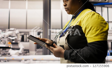 Engineer in smart solar manufacturing facility calibrating high tech machinery and analyzing sensor data. Engineer troubleshooting photovoltaic assembly equipment, camera A close up 127155906