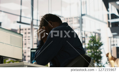 Worker feeling painful headache while working, suffering burnout while rushing to finish tasks before deadline. African american man in office having migraine after working overtime, camera A 127155907