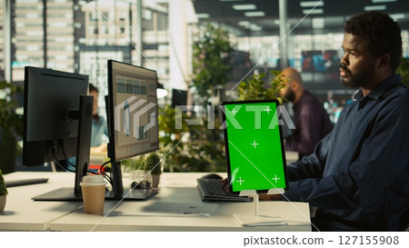Close up of green screen tablet in front of employee checking progress done on project. Chroma key device next to office clerks reading data statistics on PC screen, camera B 127155908