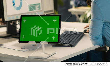 Close up of employee sitting at office desk, using green screen tablet to solve tasks during job shift. Office clerk doing email communication in workplace using chroma key device, camera A 127155936