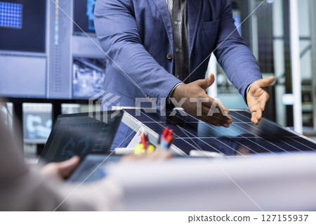 Investors examine solar panel surface, discussing design efficiency with factory management executives. Businessmen meeting with manager to chat about technical improvements to solar cells 127155937