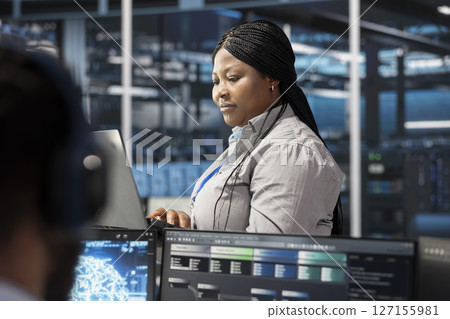Data center software developer using artificial intelligence neural networks tech. African american server farm employee using AI programming language on computer, configuring specialized hardware Data center software developer using artificial intelligence neural networks tech. African american server farm employee using AI programming language on computer, configuring specialized hardware 127155981