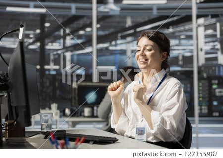 Joyous IT expert in data center office satisfied after checking report showing stable equipment performance. Happy server hub staff member relieved after successfully completing operations. 127155982