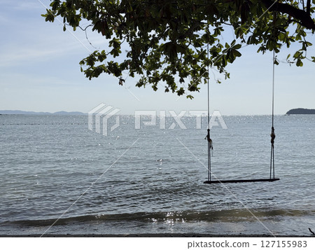 Breathtaking wooden swing found on an exotic beach in Thailand, amazing picturesque landscape of a beach front and lagoon in the evening. Lovely tropical scenery with waves crashing. 127155983