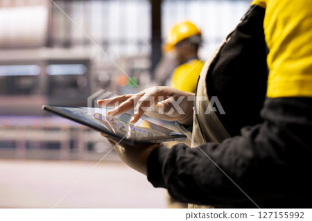 Closeup of professional using tablet in high tech factory, symbolizing industry 4.0, digital automation and real time production monitoring. African american engineer handling robotic arm maintenance. 127155992
