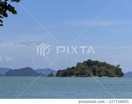Tropical landscape and beach with golden sand and blue sea waves, picturesque coastal scene featuring clear water and a peaceful shoreline with small forest islands in Thailand. 127156001
