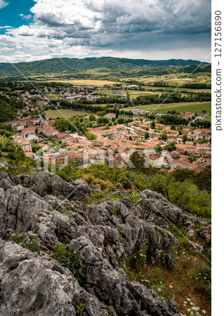 Picturesque View Of Vipava From Castle Ruins: Red-Tiled Rooftops And Church Tower Nestled In Green Valley With Blooming Flowers In Foreground And Rolling Fields In Background, Slovenia Picturesque View Of Vipava From Castle Ruins: Red-Tiled Rooftops And Church Tower Nestled In Green Valley With Blooming Flowers In Foreground And Rolling Fields In Background, Slovenia 127156890