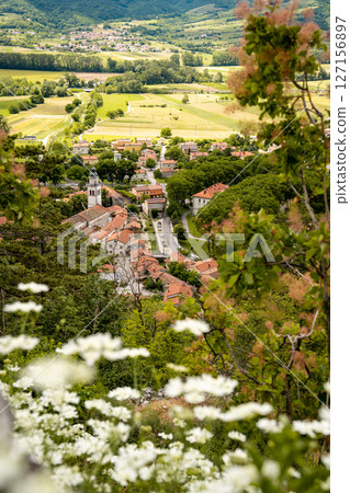 Picturesque View Of Vipava From Castle Ruins: Red-Tiled Rooftops And Church Tower Nestled In Green Valley With Blooming Flowers In Foreground And Rolling Fields In Background, Slovenia Picturesque View Of Vipava From Castle Ruins: Red-Tiled Rooftops And Church Tower Nestled In Green Valley With Blooming Flowers In Foreground And Rolling Fields In Background, Slovenia 127156897