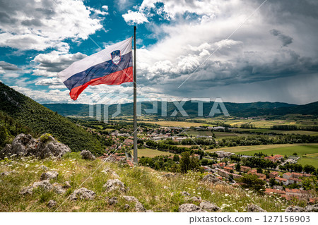 Slovenian Flag Flying Over Vipava Valley: Panoramic View Of Town And Countryside Framed By Mountains And Dramatic Clouds Under A Windy Summer Sky In Western Slovenia Slovenian Flag Flying Over Vipava Valley: Panoramic View Of Town And Countryside Framed By Mountains And Dramatic Clouds Under A Windy Summer Sky In Western Slovenia 127156903