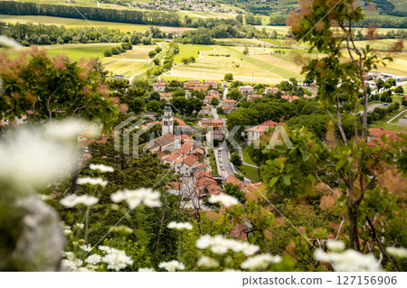 Picturesque View Of Vipava From Castle Ruins: Red-Tiled Rooftops And Church Tower Nestled In Green Valley With Blooming Flowers In Foreground And Rolling Fields In Background, Slovenia Picturesque View Of Vipava From Castle Ruins: Red-Tiled Rooftops And Church Tower Nestled In Green Valley With Blooming Flowers In Foreground And Rolling Fields In Background, Slovenia 127156906