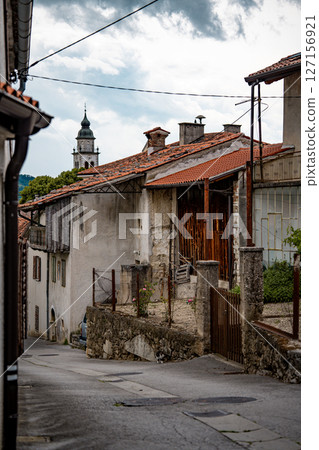 Rustic Street Scene In Vipava, Slovenia: Old Stone House With Wooden Doors And A Bench Beneath Overhanging Green Vines Along A Quiet Winding Lane In The Countryside Rustic Street Scene In Vipava, Slovenia: Old Stone House With Wooden Doors And A Bench Beneath Overhanging Green Vines Along A Quiet Winding Lane In The Countryside 127156921