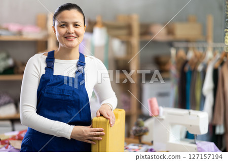 Positive young repairwoman holding tools case in tailor's workshop 127157194
