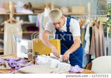 Professional young repairman master repairing sewing machine in fashionable sewing studio or sewing workshop 127157223