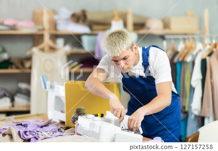 Skilled young repairman repairing sewing-machine Skilled young repairman repairing sewing-machine 127157258