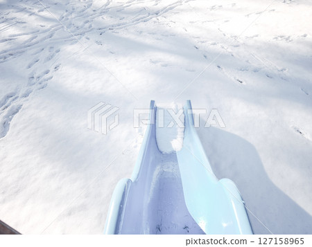 Light blue slide partially covered in snow, set in a wintery playground in aosta, italy. Footprints create patterns in the surrounding snow Frazionne Lillaz 127158965